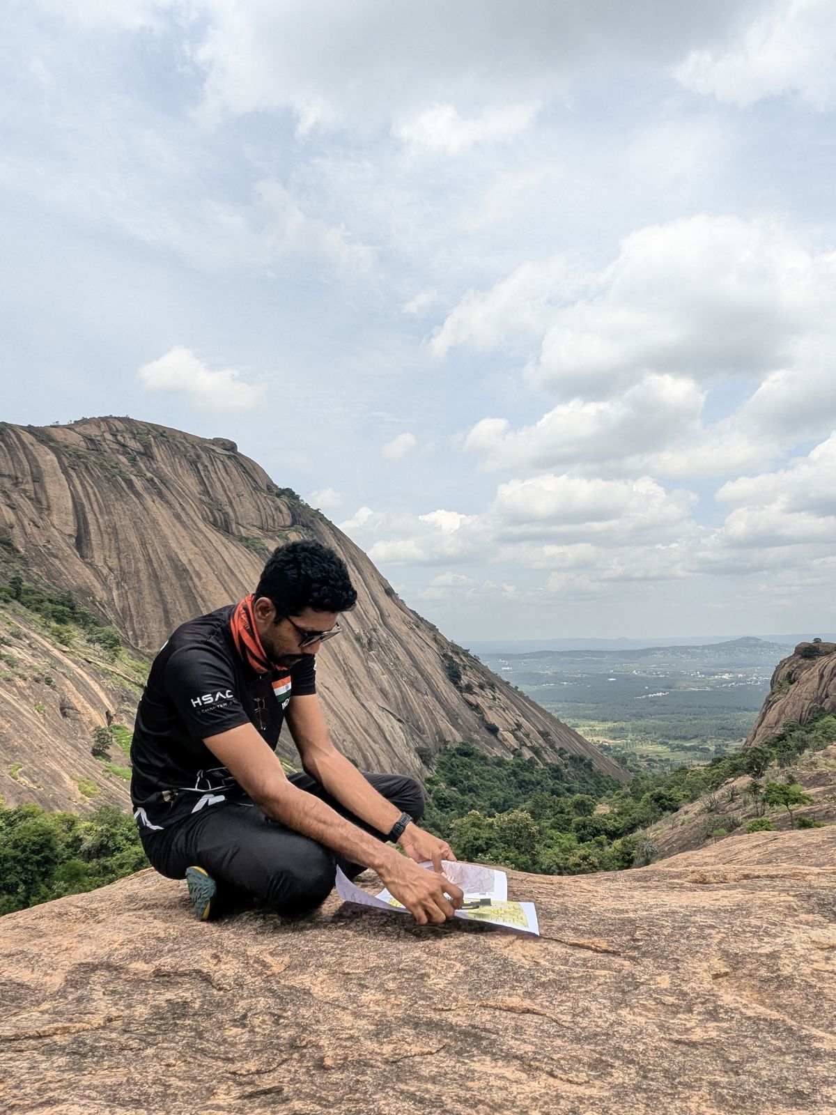 Manoj reading a topographic map with a compass on a granite summit